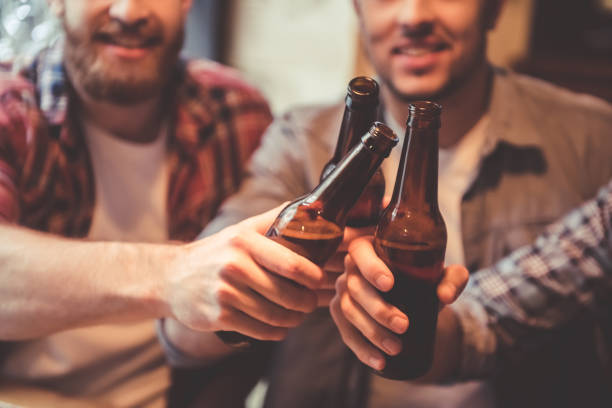 Cropped image of handsome friends clinking bottles of beer and smiling while resting at the pub