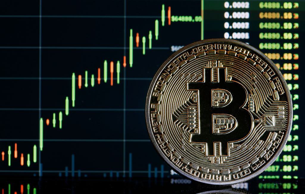 PARIS, FRANCE - OCTOBER 21: In this photo illustration, a visual representation of the digital Cryptocurrency, Bitcoin is on display in front of the Bitcoin course's graph on October 21, 2021 in Paris, France. The value of Bitcoin (BTC) has exceeded the threshold of 66,895 dollars for the first time in his history. Cryptocurrency, which traded for less than a dollar 12 years ago, peaked on Thursday at around $ 66,895, its all-time high. Bitcoin has increased by over 50% over one month and over 450% over one year. (Photo illustration by Chesnot/Getty Images)