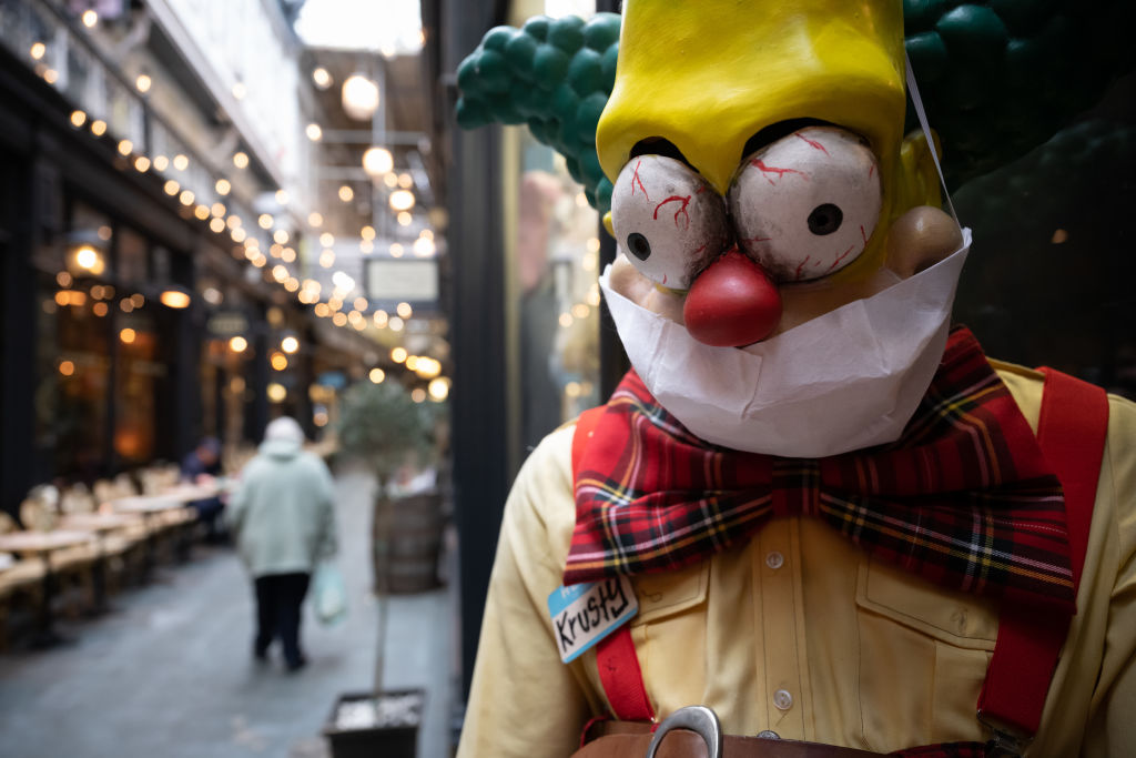 CARDIFF, UNITED KINGDOM - MARCH 18: An elderly woman walks passed a Simpsons character in a surgical face mask outside a fancy dress shop on March 18, 2020 in Cardiff, United Kingdom. Coronavirus (Covid-19) has spread to over 170 countries in a matter of weeks, claiming over 8,000 lives and infecting over 200,000. There are currently 1950 diagnosed cases in the UK and 71 deaths. (Photo by Matthew Horwood/Getty Images)