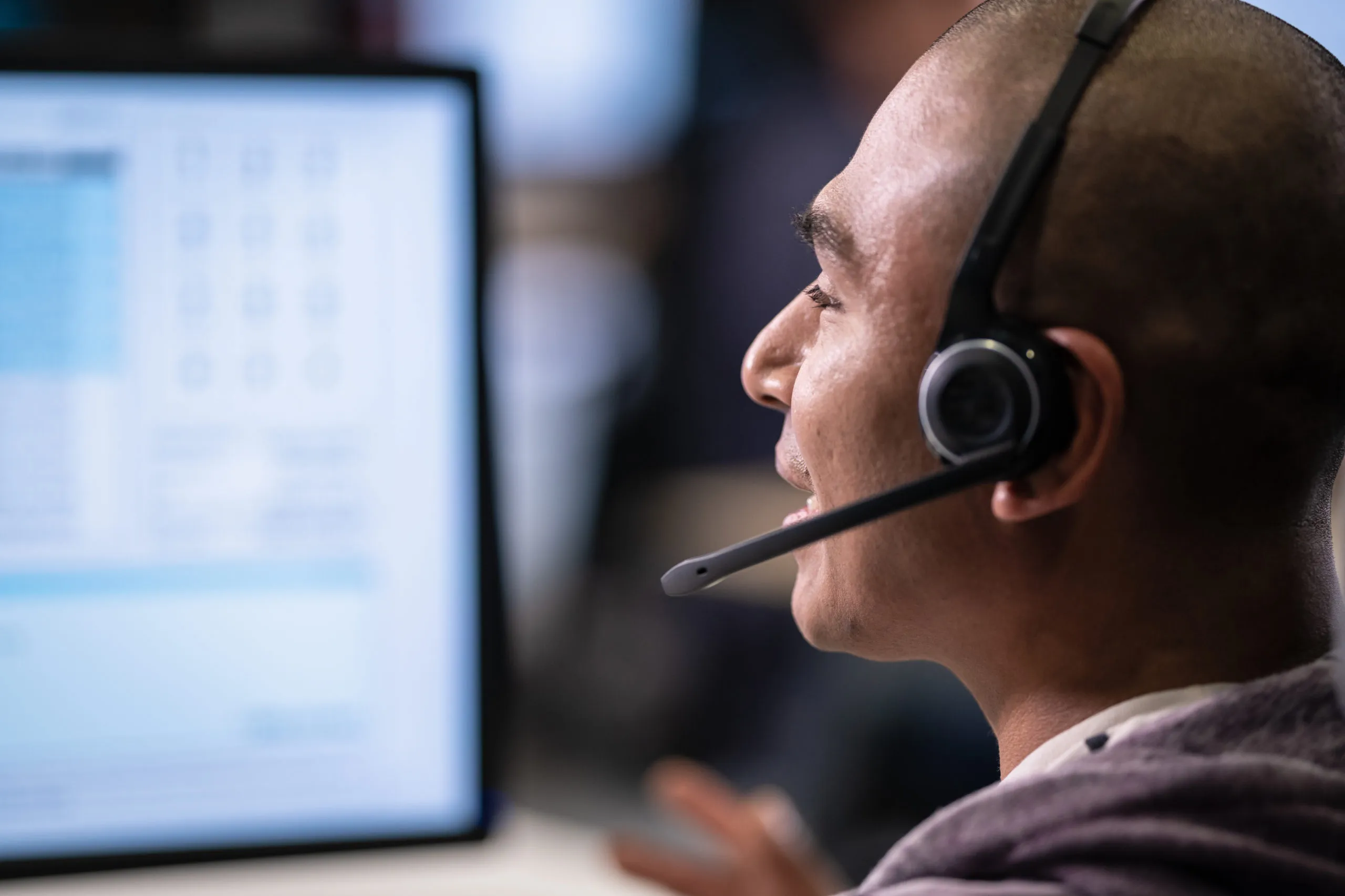 Hispanic man using a computer and talking to a customer over a headset while doing customer support in a call centre.