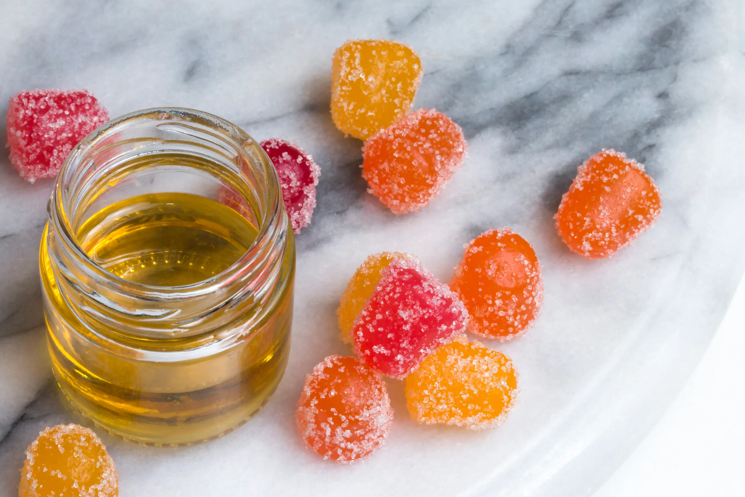 CBD gummy candy gumdrops and oil on a white marble surface