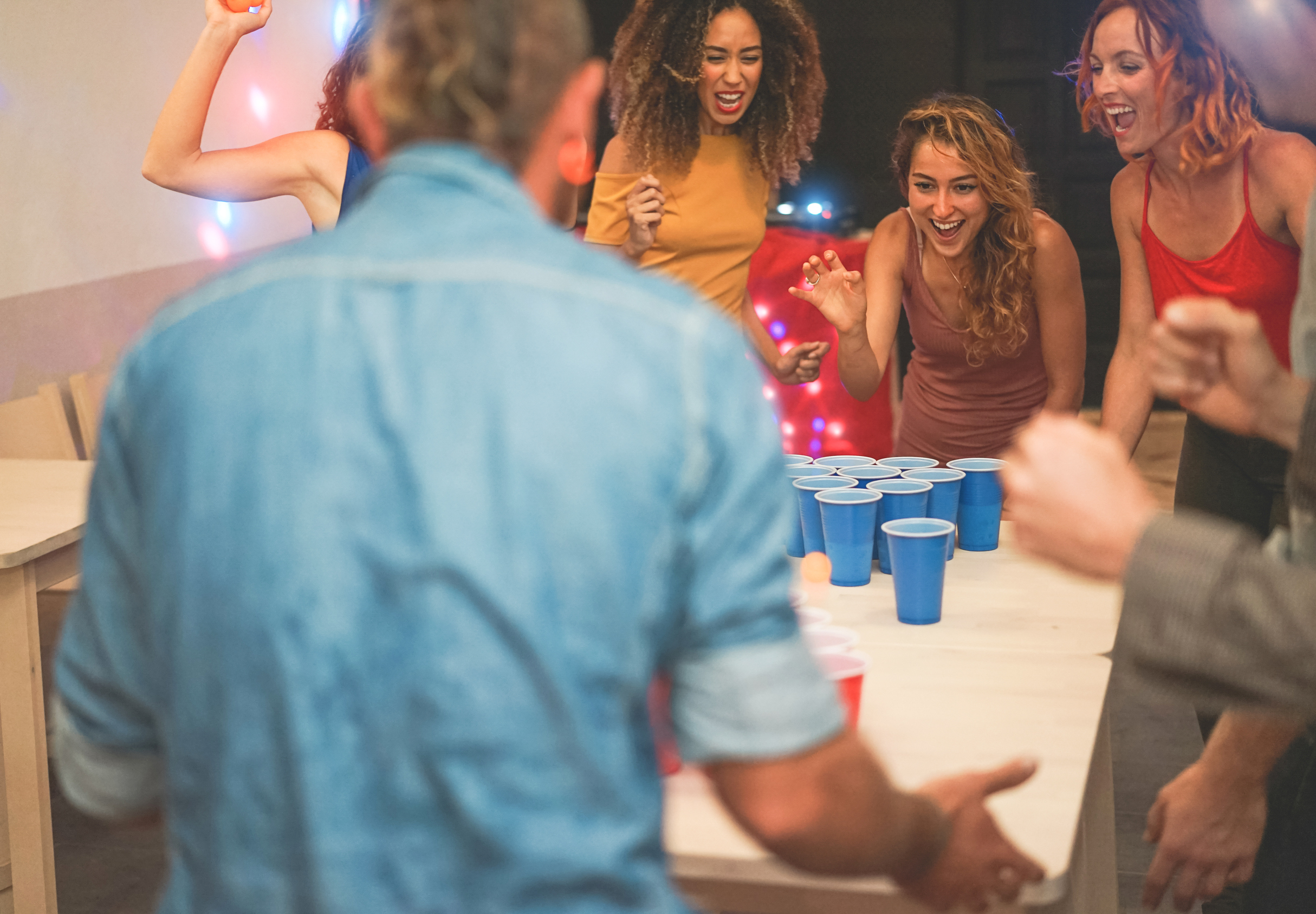 Group of happy friends playing beer pong in pub cocktail bar - Young millennials people having fun doing party at night - Friendship, fest and nighlife concept - Focus on center girl face