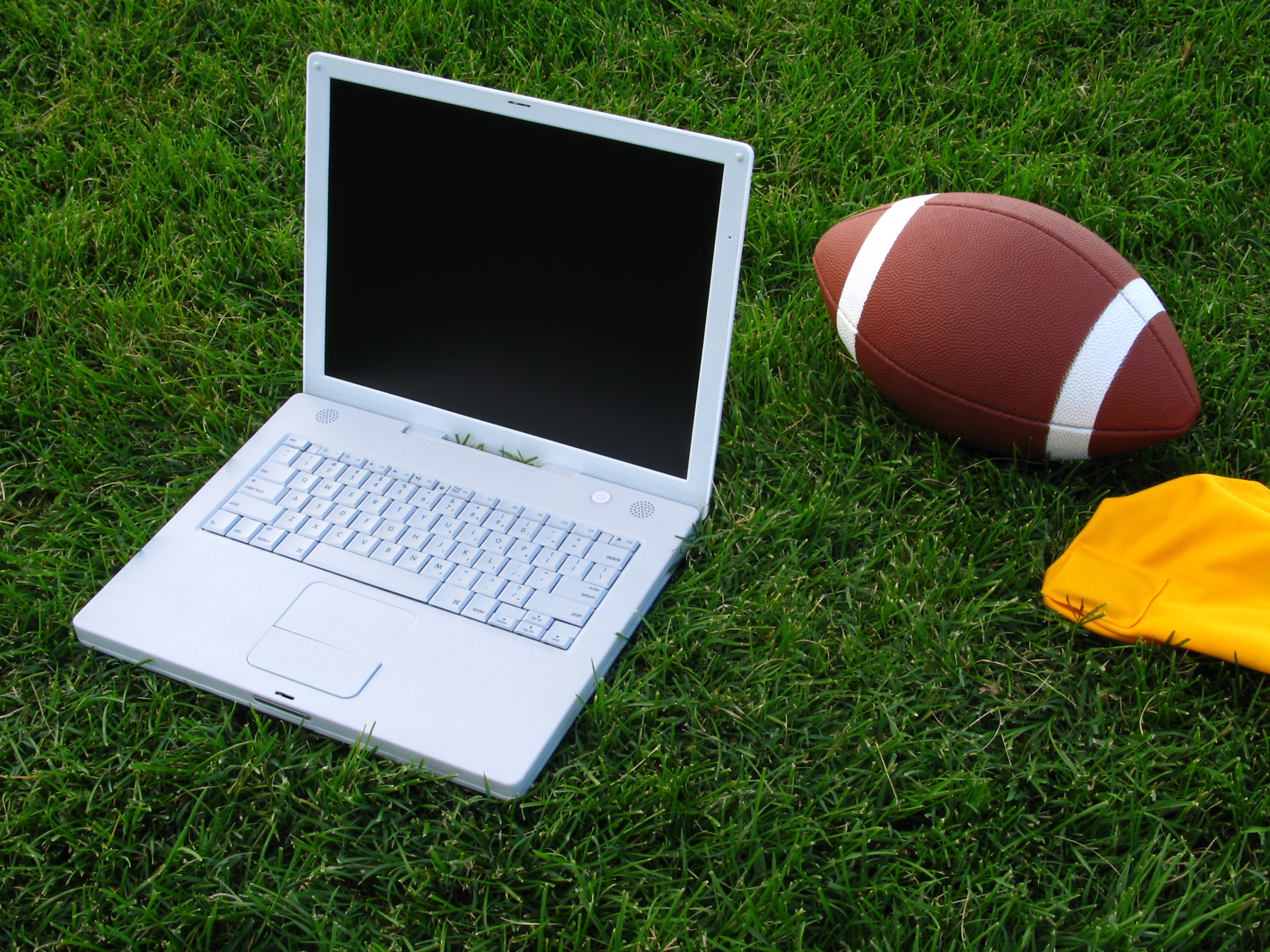 Fantasy Football Concept: Laptop Computer and Football on Grass Field