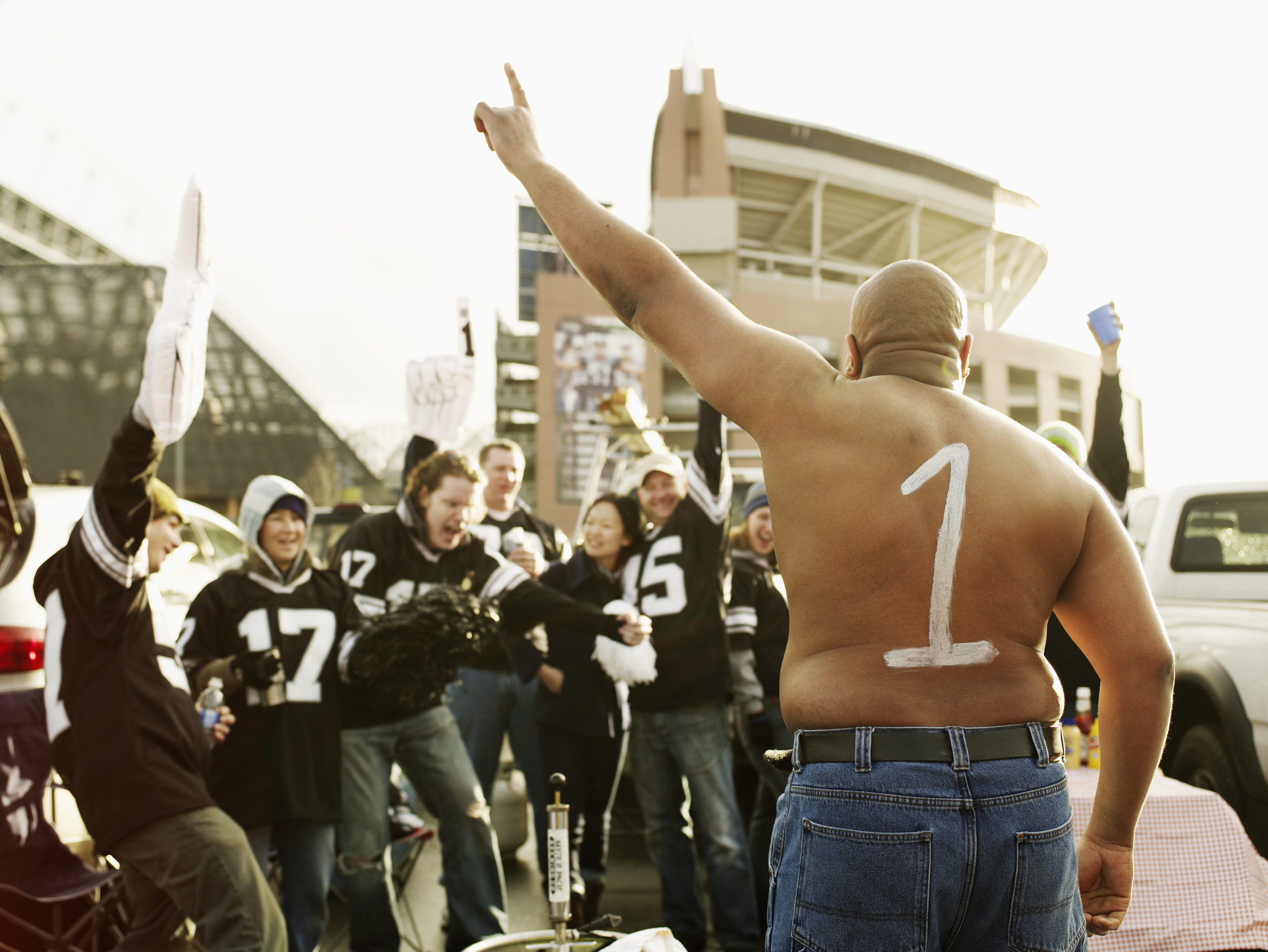 Man with '1' painted on back cheering with friends at tailgate party