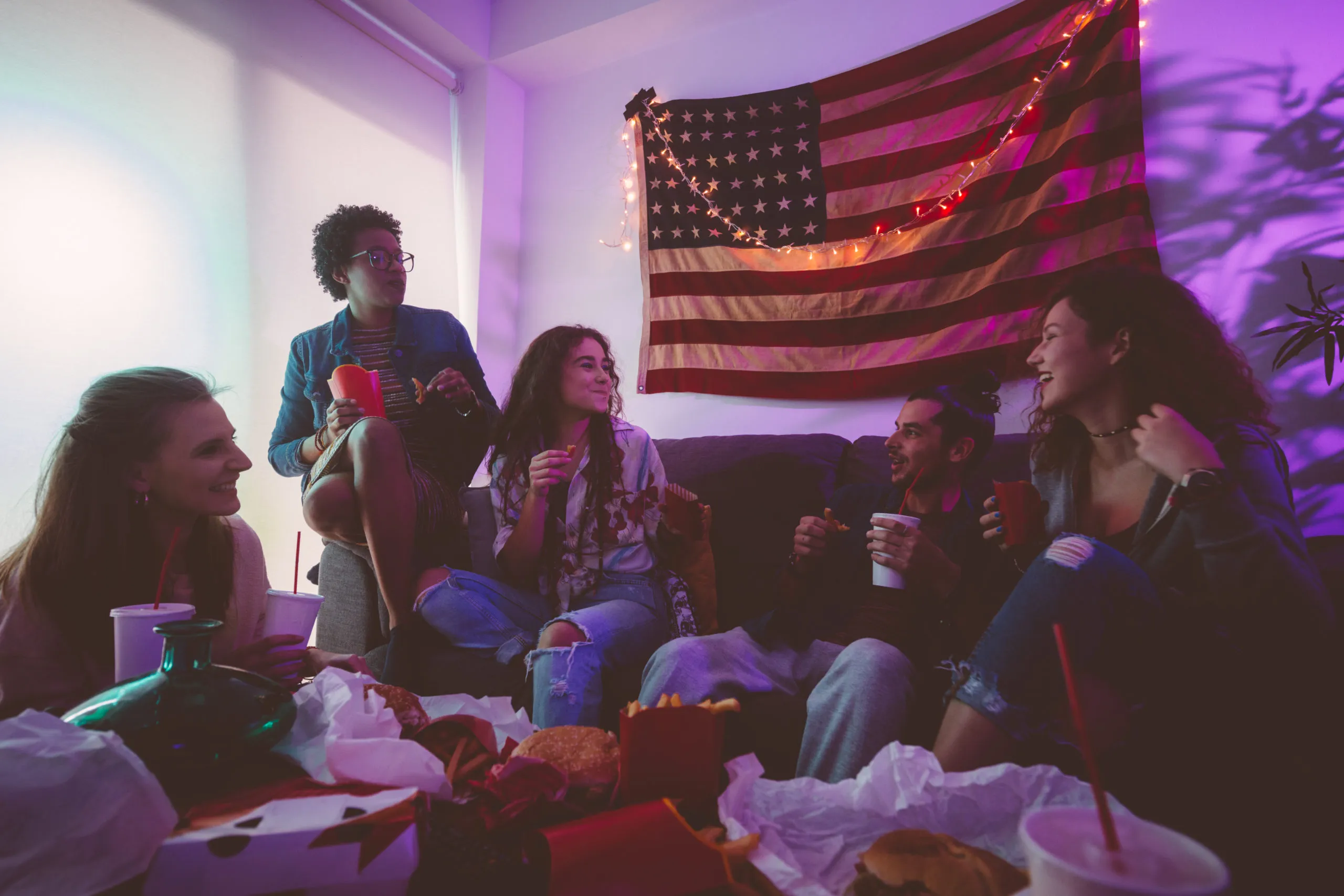 Happy multi-ethnic teenage friends hanging out at home and eating fast food together