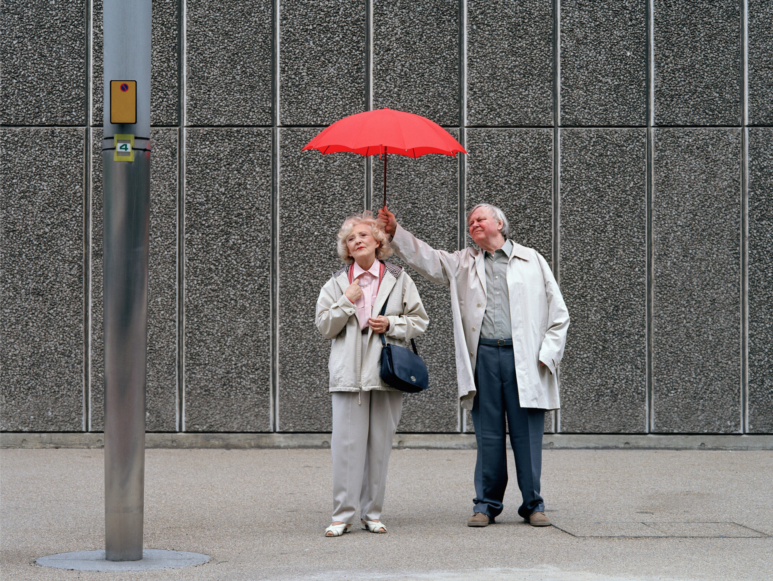 Senior man holding red umbrella over woman, standing on pavement