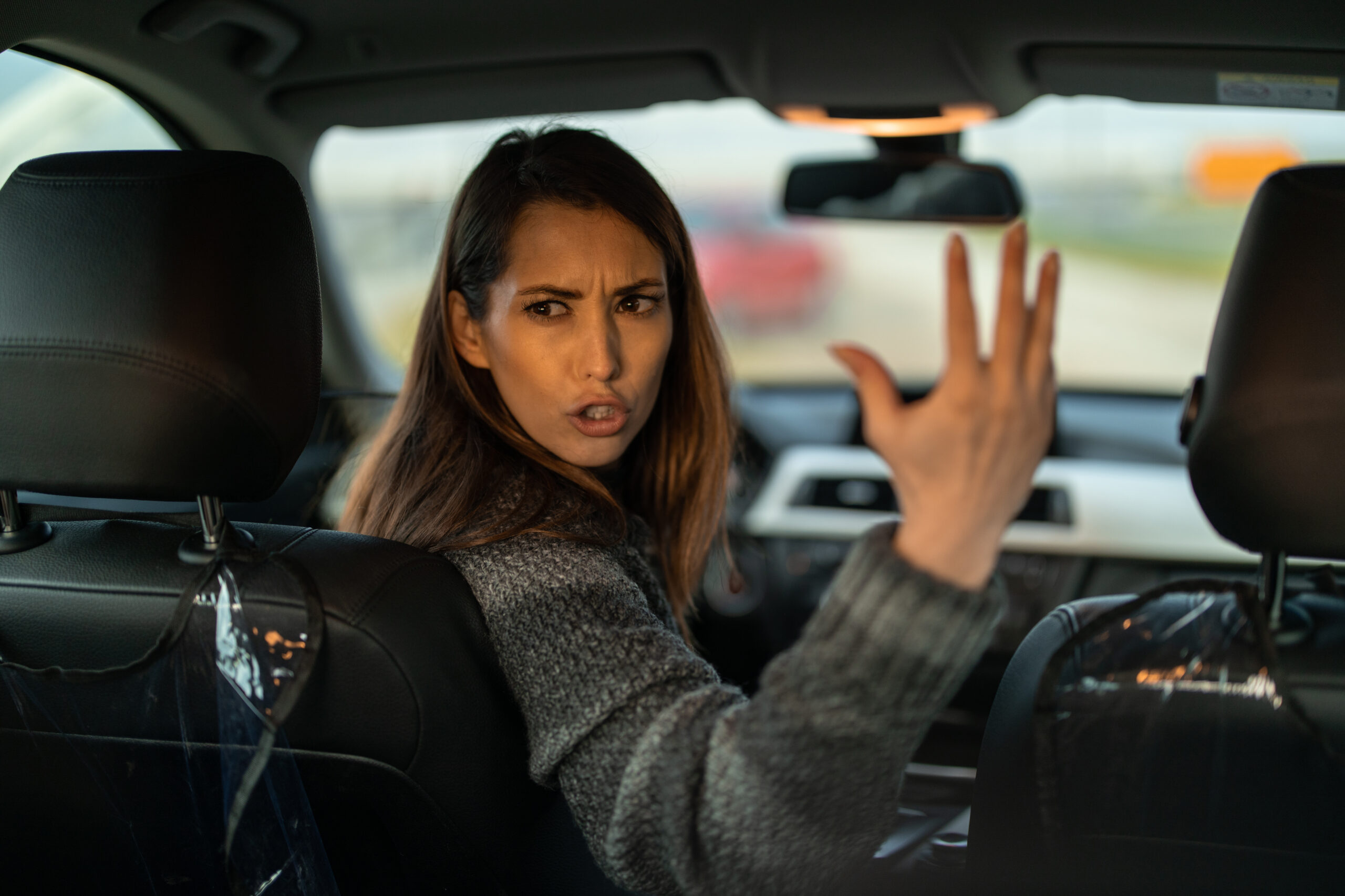 Angry displeased woman sitting in car, looking over shoulder and shouting