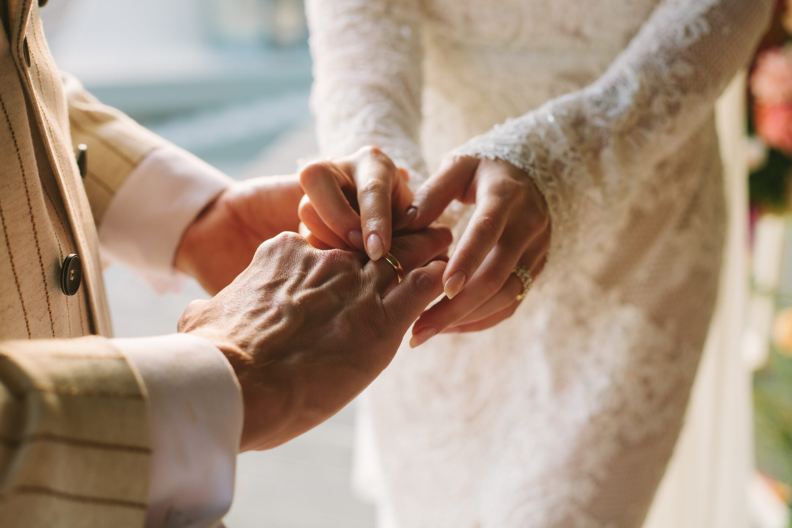 Bride putting ring on groom's finger. Rings exchange. Happy couple celebrating wedding outdoors in summer.