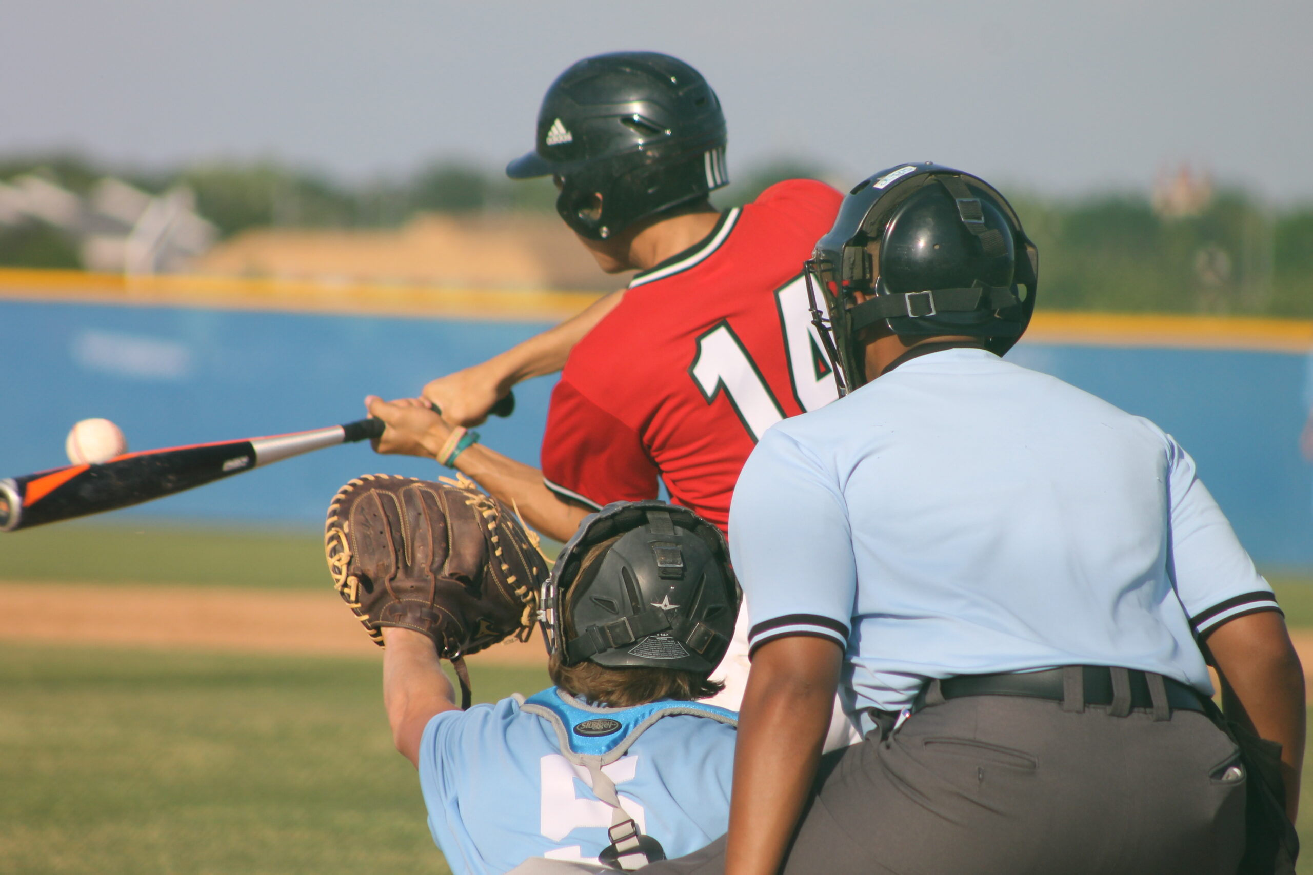 Junior varsity high school baseball player at bat connects with the baseball
