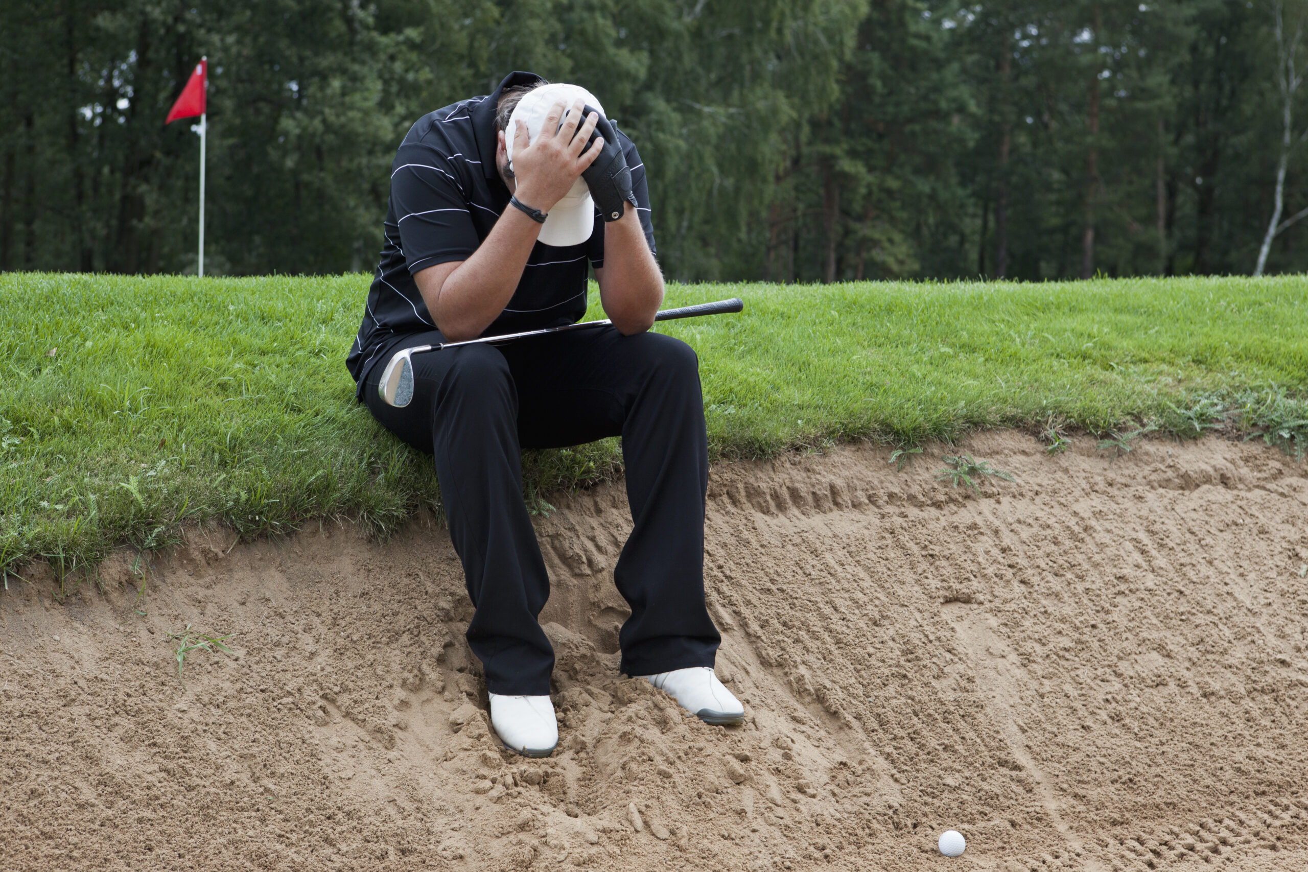 A golfer sitting at the edge of sand trap, head in hands