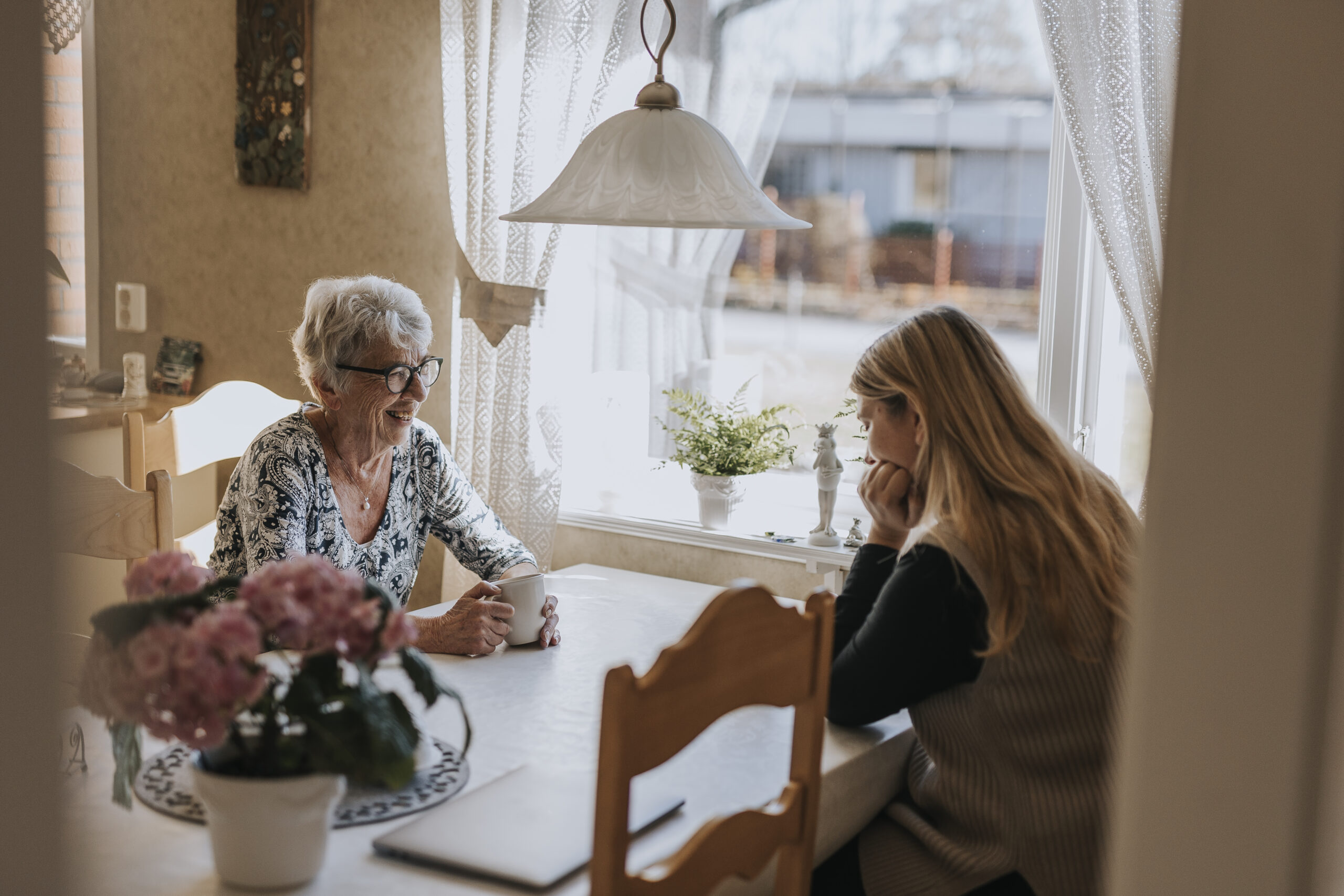 Grandmother and adult granddaughter sitting at table and having tea