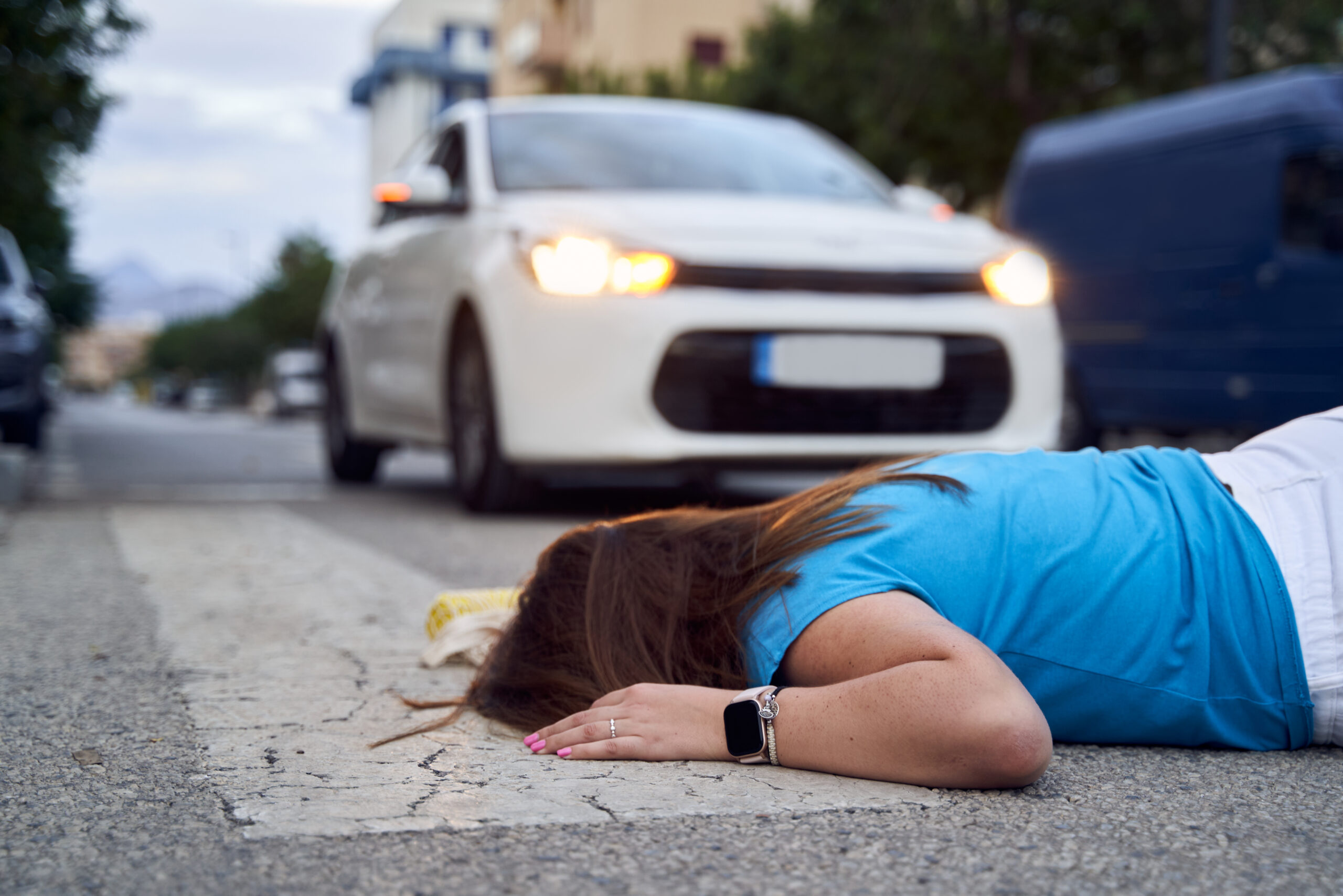 Side view of an unrecognizable young woman lying on the ground at a crosswalk after being hit by a car.