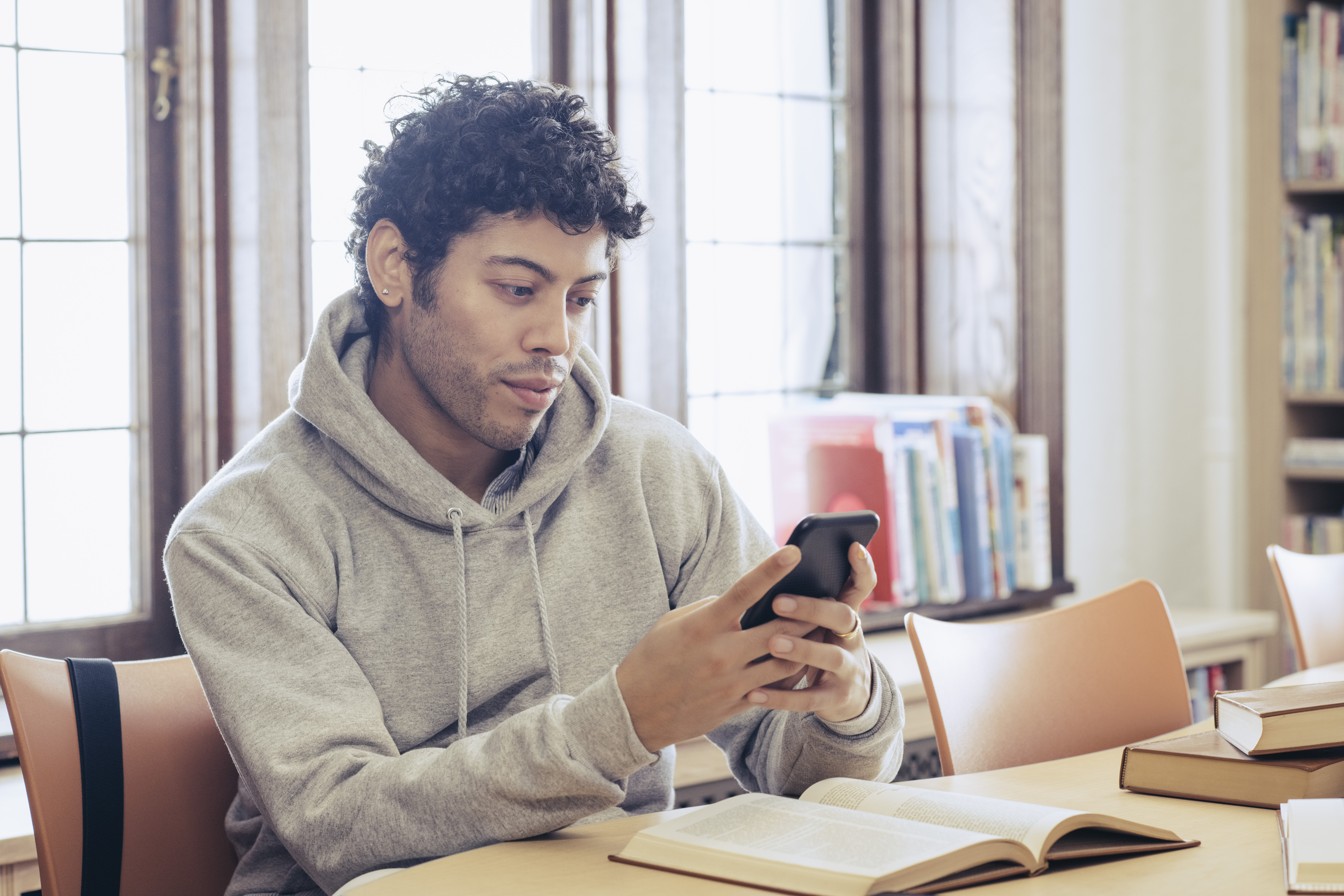 Young man looking at smart phone while studying in library