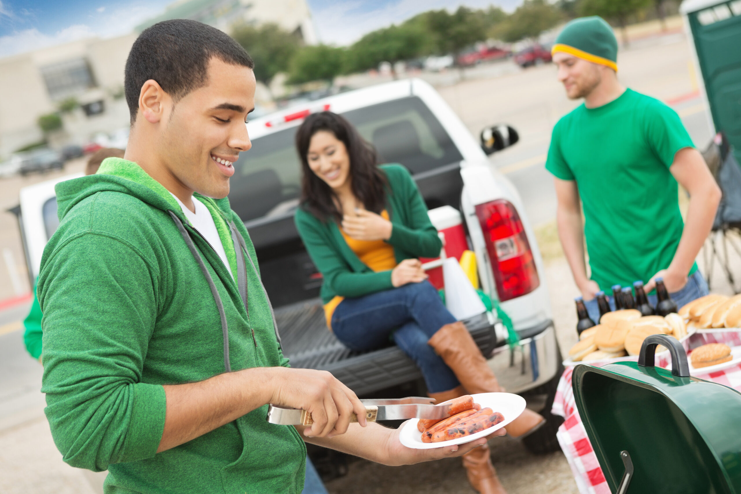 Young man grilling during tailgating party near football stadium