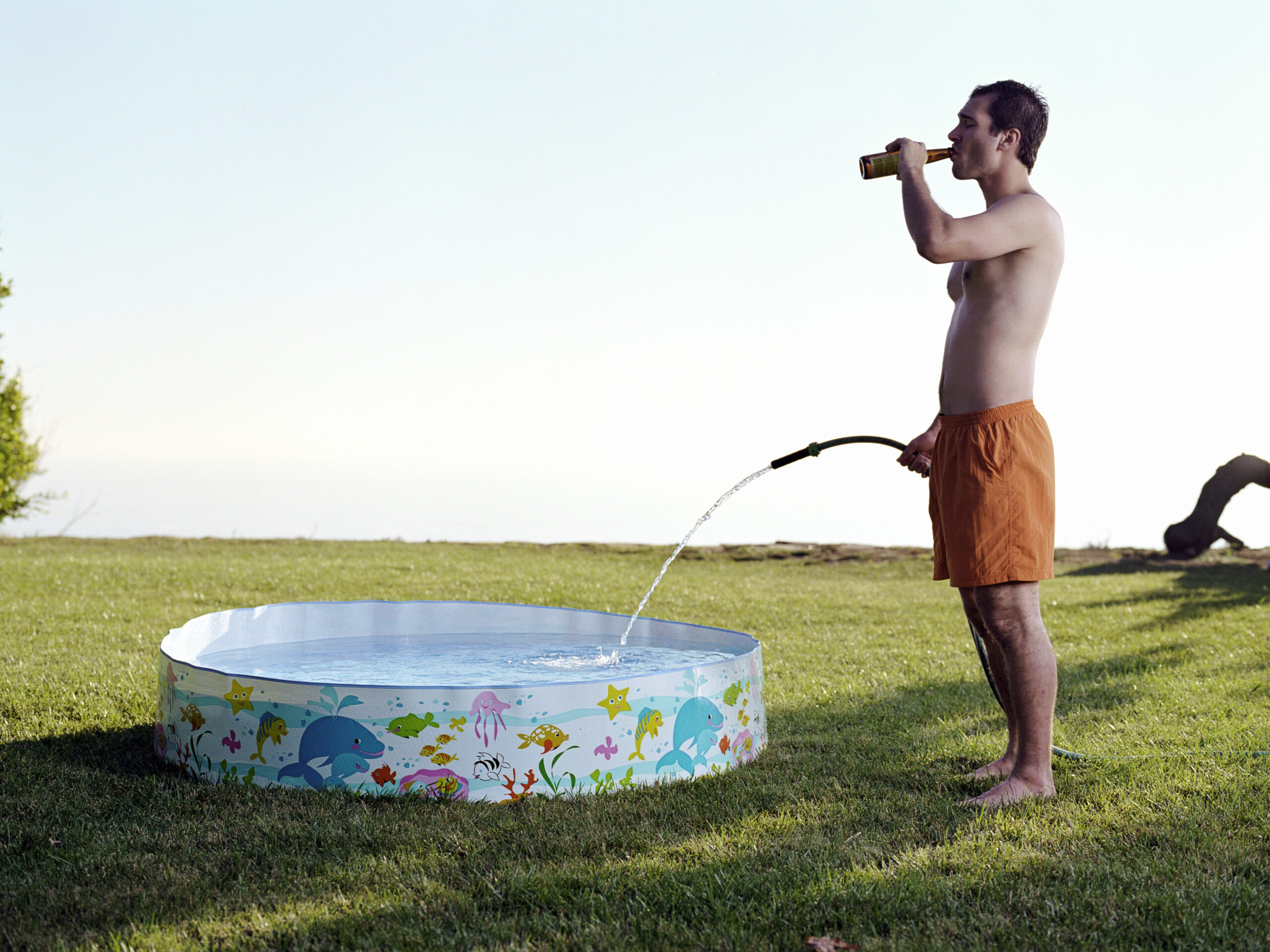 Young man filling plastic pool with water from hose